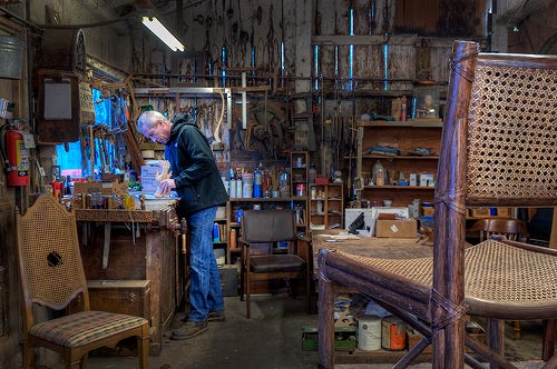 The workshop interior with caned chairs in the foreground and tools covering the walls.