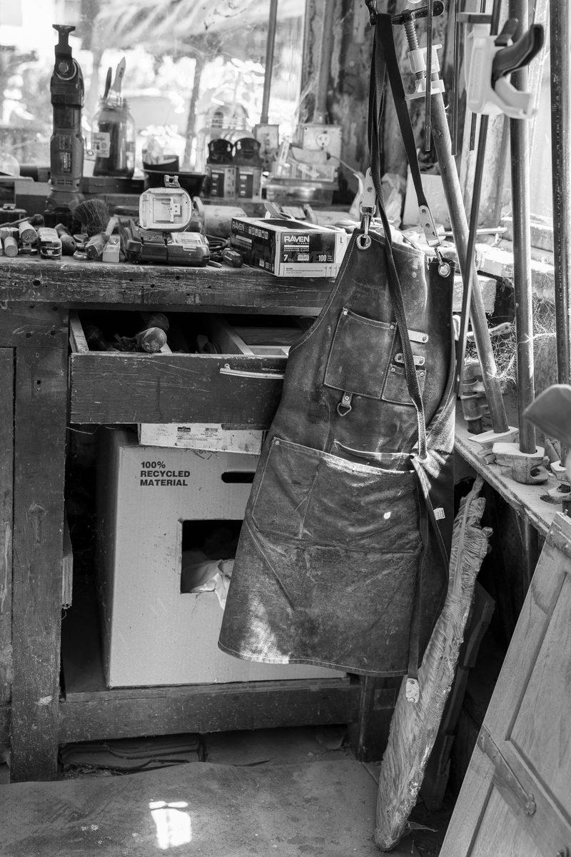A worn leather apron hanging beside a cluttered workbench.