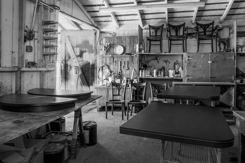 The workshop interior: tabletops laid across trestles in the foreground, chair frames hung along the far wall.
