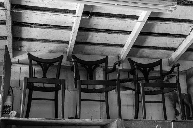 Three stripped chair frames standing side by side on a shelf under the barn rafters.