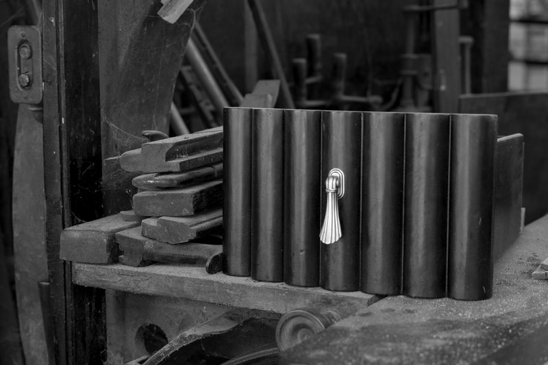 A reeded cabinet front with a single brass teardrop pull, resting on a bench next to a row of chisels.